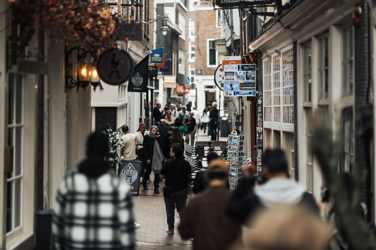 The Local Businesses Winning Right Now Aren't the Best — They're the Most Visible People walking through a narrow urban alley with shops and signs on both sides.
